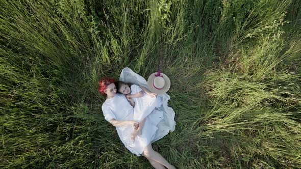 Mom and Daughter in White Clothes Dresses Lie on a Field alt