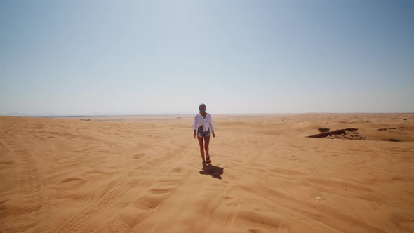 Front View of Young Woman in Sunglasses and Scarf Over Her Head Walking in the Desert Near Dubai alt