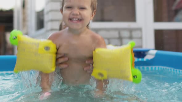Mom Plays with a Naked Baby in Oversleeves in the Pool Against the Background of a Summer Sunset alt