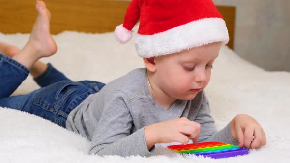 Little boy lies and plays an educational game in Santa hat. Colorful antistress sensory toy