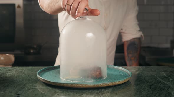 Male Hand Lifts To Up Glass Cloche From a Plate with Hot Food Beef Steak and Moving Smoke at the alt