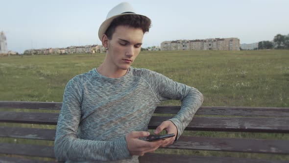 Guy Sits on an Old Wooden Bench with a Phone Looks Around in Anticipation Camera Tracking alt