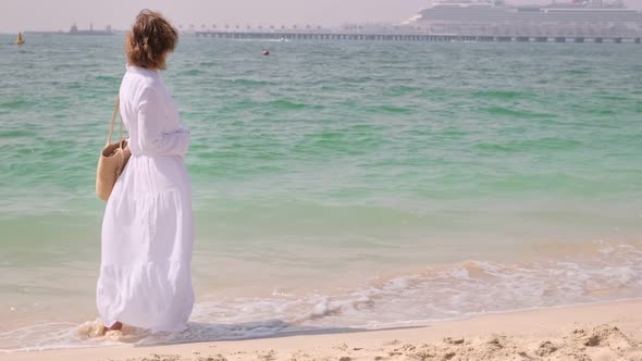 Young White Dressed Woman is Standing on the Sandy Coast Close to the Blue Sea