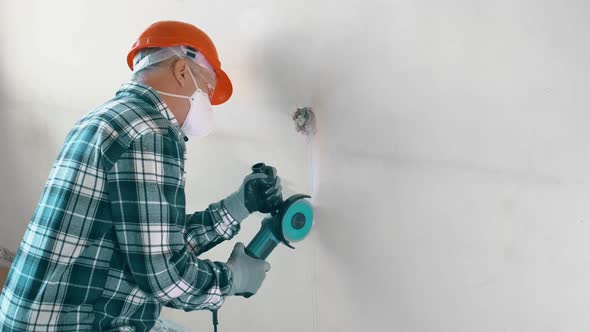 An Elderly Worker in an Orange Helmet and Protective Glasses with an Angle Grinder for Cutting Metal