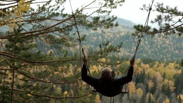 A Man Flies High Swinging on a Swing in the Woods
