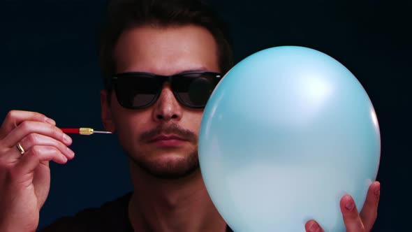 European Man in Sunglasses Bursts Blue Balloon with a Dart