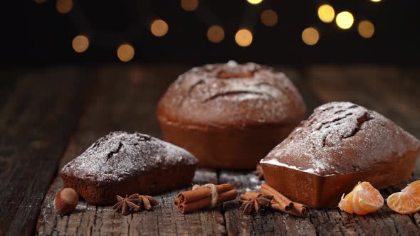 Three Christmas Bread Stollen on a Wooden Textured Table Against the Background of Blurred Lights in alt