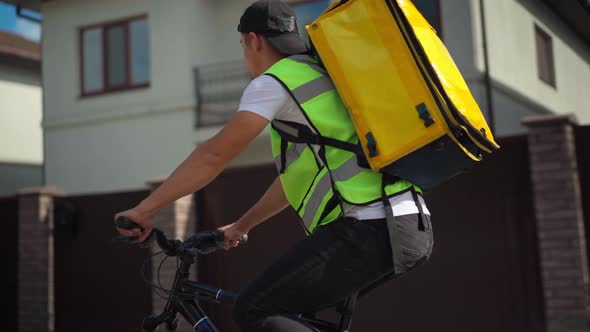 Young Man with Delivery Bag Riding Bike Looking Around Searching Client Address alt