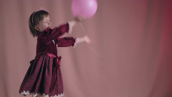 Cute Little Girl in Vintage Burgundy Dress is Playing with Pink Inflatable Ball