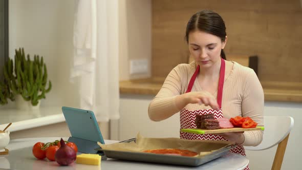 Female Chef Preparing a Pizza and Watching Recipes Online on Platform for Watching Videos on Your alt