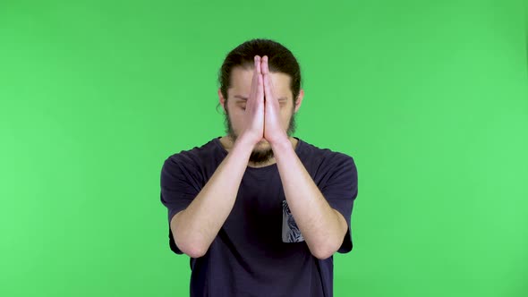 A Darkhaired Young Man in a Black Tshirt Holds His Palms Together in a Prayer Gesture alt