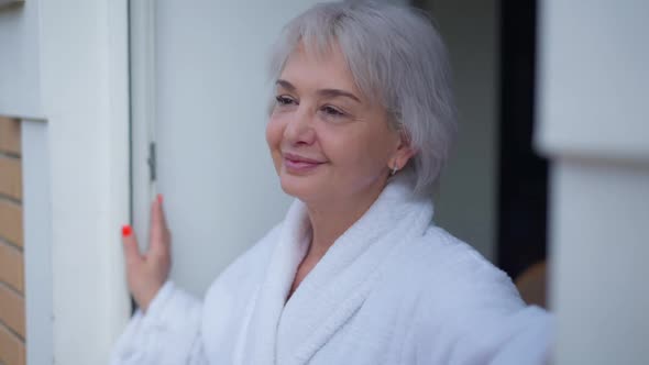 Cheerful Caucasian Mature Woman with Brown Eyes Smiling Standing at Doorway Looking Out alt
