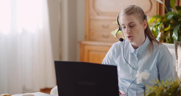 Sales Representative in Headset Speaking To Client and Making Video Conference Call on Laptop alt