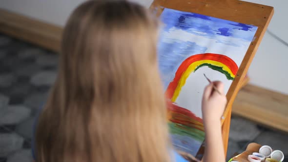 A Preschooler Girl Draws a Picture on an Easel