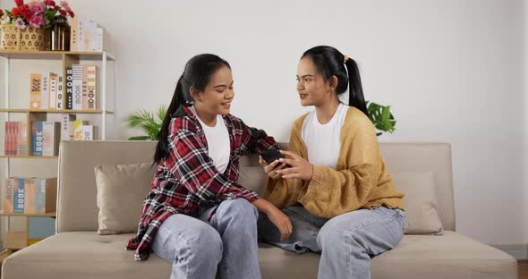 Twin girls sitting on couch and shopping online with smartphone at living room alt