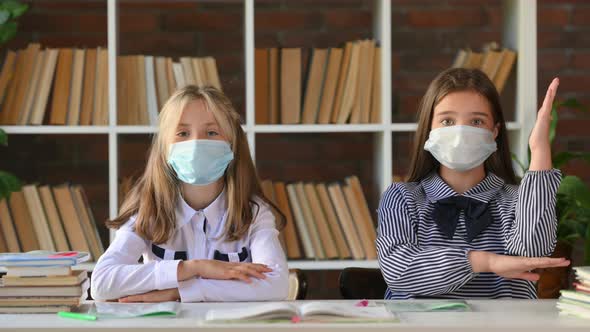 Portrait of young schoolgirls in protective masks sitting at a desk