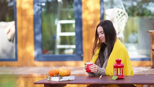 Happy Young Woman with Phone and Drinking Coffee Sitting at the Wooden Table Outdoors