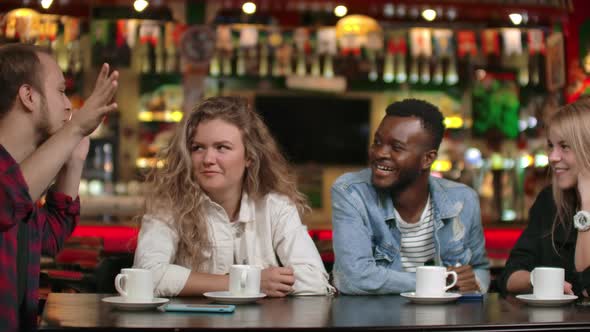Student Meeting in a Restaurant and Cafe. A Man in a Shirt Tells a Story To Friends, Two Girls and alt