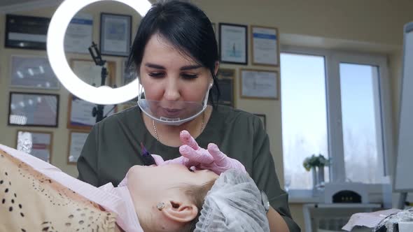 Cosmetologist Wearing a Mask and Gloves Applies Permanent Makeup to the Lips of a Young Girl