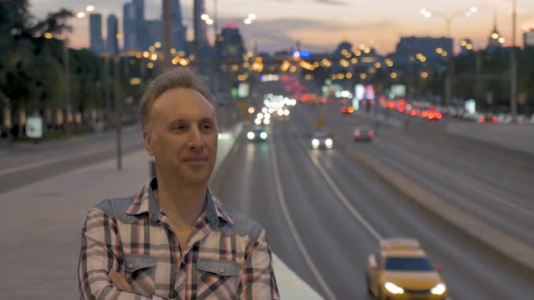 Man Enjoys City View Against Street and Buildings at Sunset alt