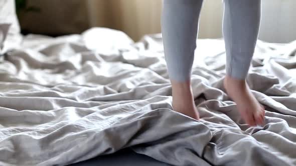 Happy little girl jumping on the bed and falling in the morning. childs feet on blanket close