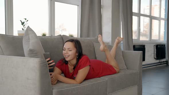Attractive Woman Is Lying on Couch, Smiling and Talking with Family.