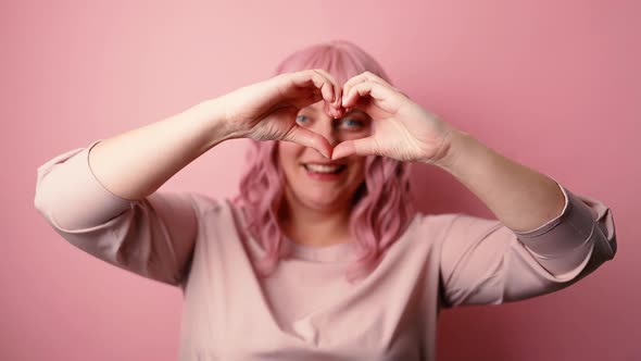 Charming Woman 20s Shapes Heart Gesture Looking at Camera Isolated on Pink Background