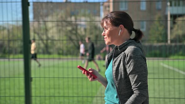 Active Mature Woman in Sportswear with Smartphone Outdoor Profile View alt