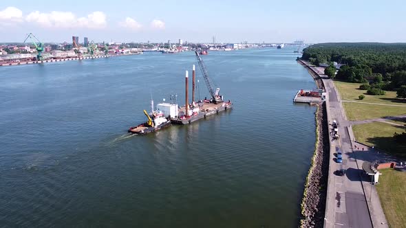 Tugboat pushing barge with crane on top to docks of Klaipeda harbor, aerial view alt