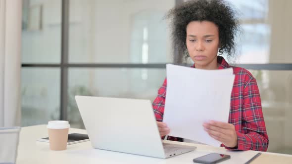 African Woman with Laptop Reading Documents in Office alt