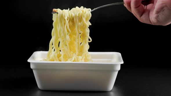 Hand with Fork Stirring and Cooling Cooked Instant Noodles