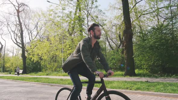 Tracking Shot of Hipster Man Riding Fixed Gear Bicycle in Park Slow Motion alt