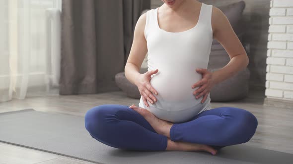 A Calm Pregnant Woman Holds Her Hands on Her Stomach Meditating on the Floor of the House in Sports