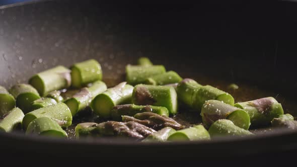 Sauteing Chopped Asparagus In A Pan, Sprinkling Salt, Black Pepper, And Garlic Powder. close up alt