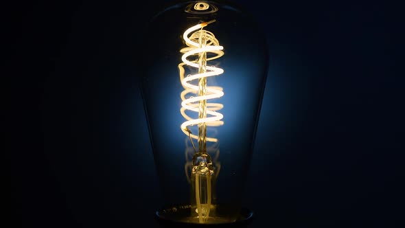 Electric Vintage Edison Light Bulb with a Spiral Flashing on a Blue Background alt
