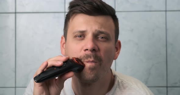 Young Man is Shaving Beard and Moustache Using Electric Razor Front View