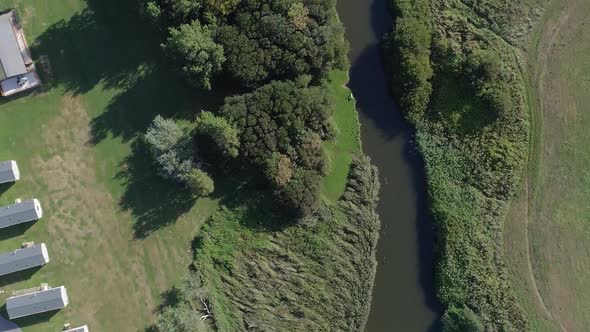 Top-down aerial of a river and the edge of a holiday caravan park. Ducks can just be made out swimmi alt