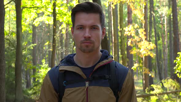 A Young Handsome Hiker Looks Seriously at the Camera in a Forest alt