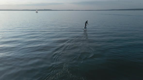 Man Riding on a Hydrofoil Surfboard on Large Blue Lake in Sunny Weather alt