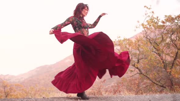 Magnificent Redhead Magic Woman Dancing in a Long Red Skirt on the Edge of the Mountains Golden alt