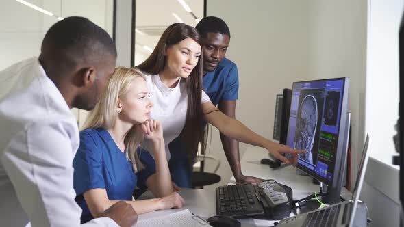 Interracial Radiologists Sitting at Table in Front of Computer Monitors and Discussing Diagnosis