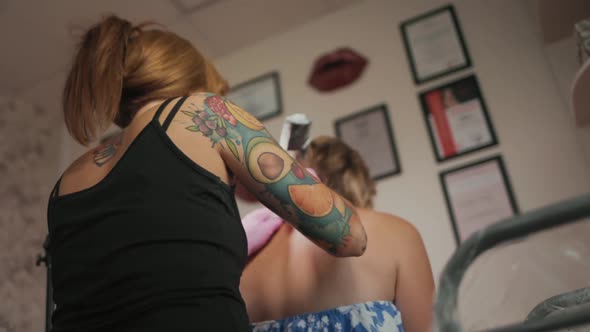 World tattoo day. Back view of master doing a tattoo on the client's back. alt