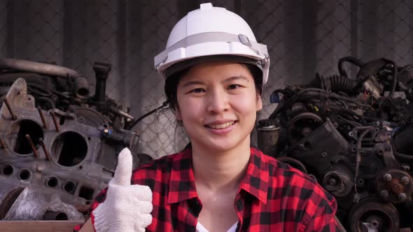 Asian female industrial worker in putting on a hard hat, putting the thumb up alt