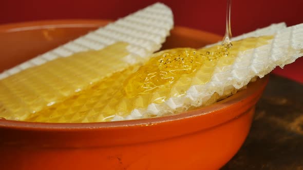 a Thin Stream of Honey is Poured Onto Waffle Pieces in a Clay Red Bowl