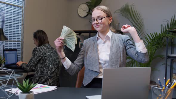 Smiling Young Business Woman Waving with Stack of Money Dollar Cash at Office Desk Workplace alt