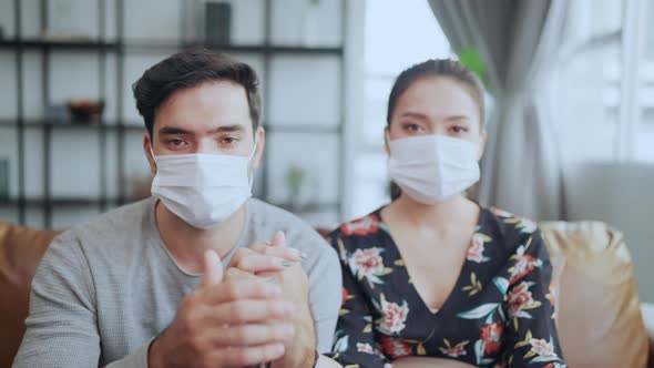 caucasian and asian marry couple wearing face mask at home feeling sad depressed about epidemic