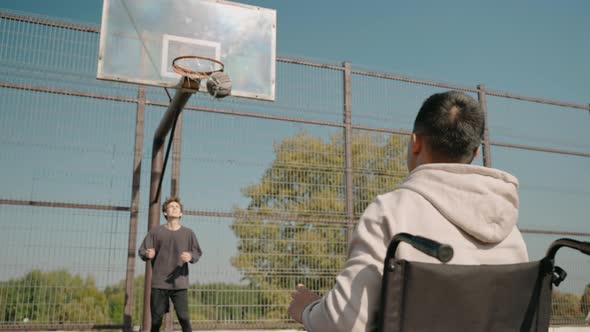 Disabled Man in Wheelchair Playing Basketball Outside with His Friend