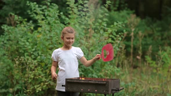 A little girl makes a fire in the grill. Family picnic in the Park.