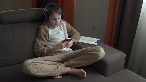 Teen Boy Listens To Music Sitting on the Couch. He Takes Off His Headphones and Picks Up a Book
