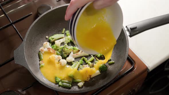 Female Hands Adds a Scrambled Eggs to Fried Vegetables While Cooking Omelette alt